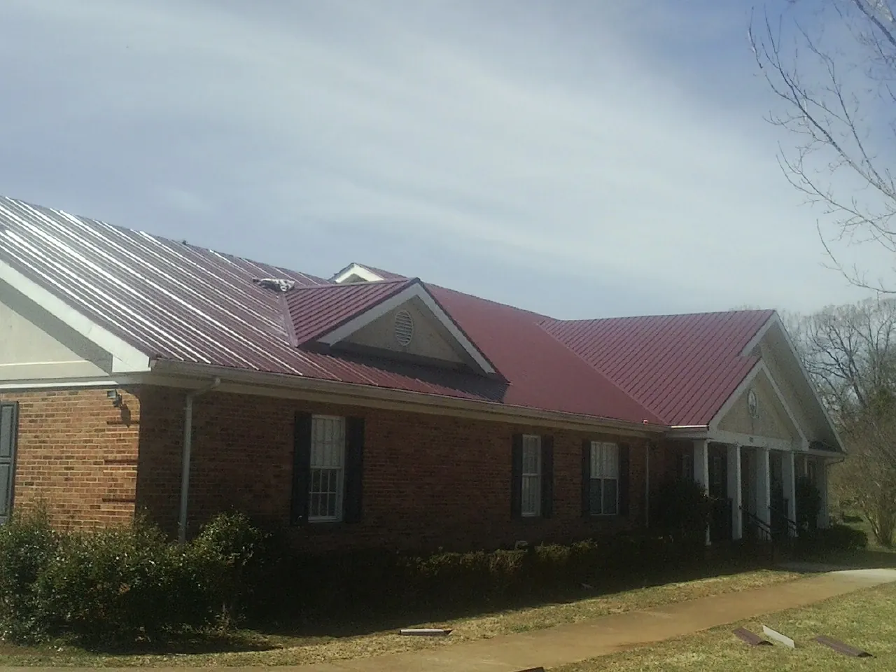 Red metal roof with gabled entries on a long brick building, from a Hail Damage Roof Repair job in Yountville
