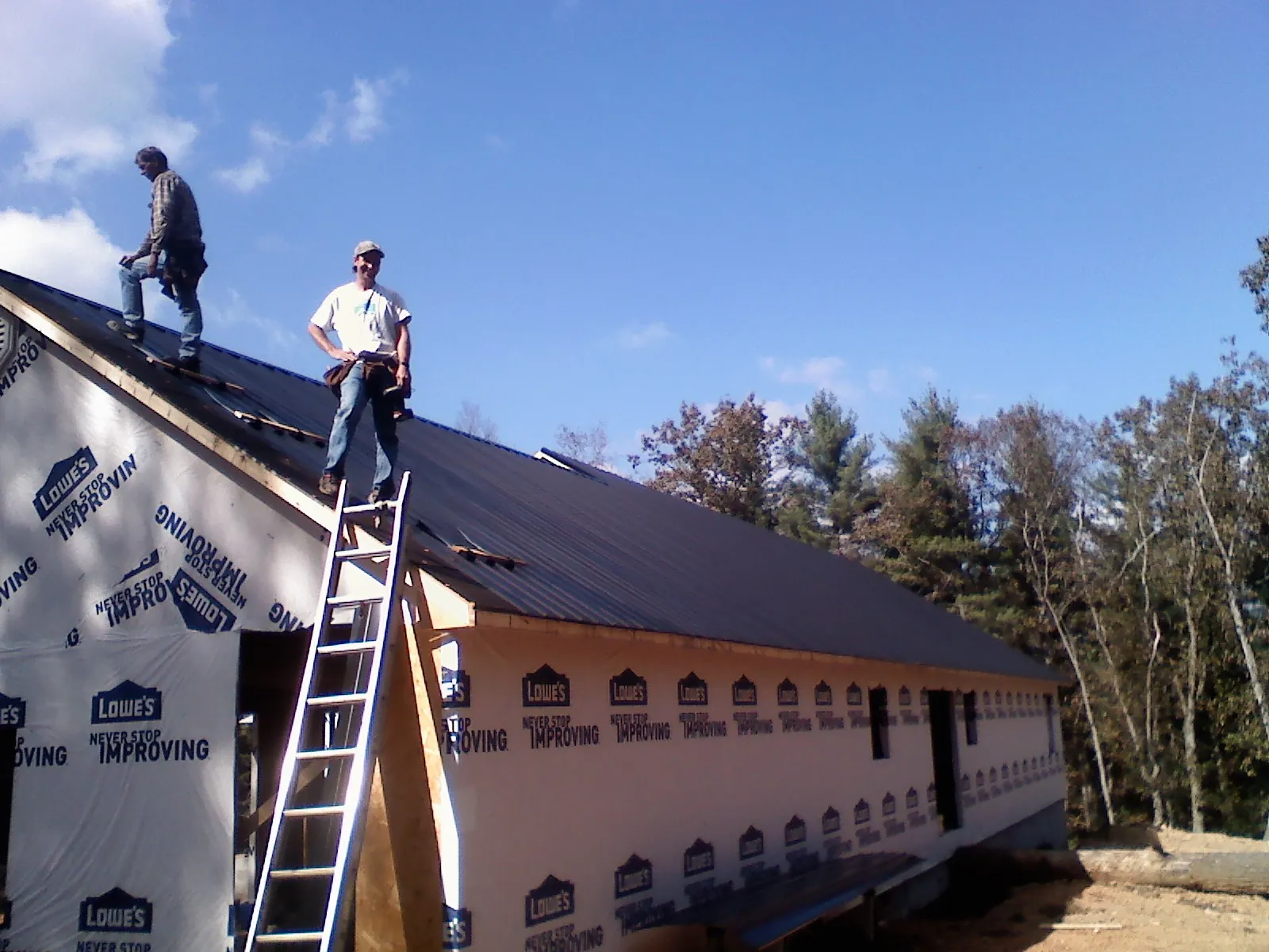 Two roofers standing on a long dark metal roof over a wrapped building in Yountville